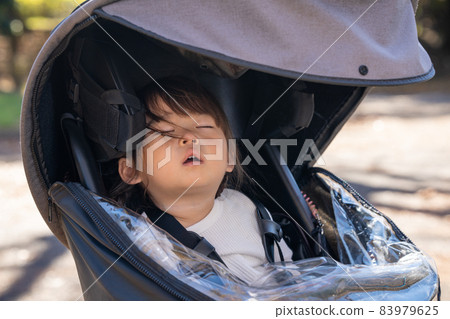 Girl sleeping in a stroller tired of playing Girl sleeping in a stroller tired of playing 83979625