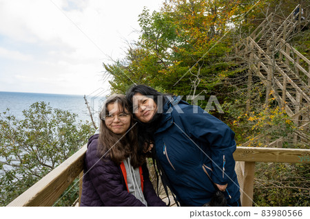 A mother and daughter smile at the camera on a wooden balcony A mother and daughter smile at the camera on a wooden balcony 83980566
