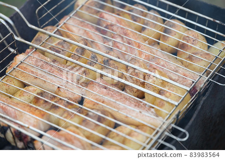 Raw vegetable and slices of meat cooking on grill outdoors Raw vegetable and slices of meat cooking on grill outdoors 83983564