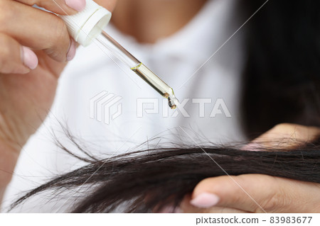 Girl hold dropper with castor extract oil near hair and apply one drop 83983677