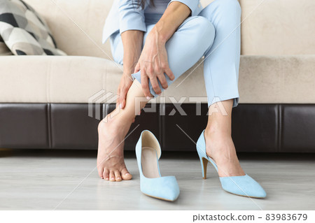 Tired woman takes off uncomfortable high heeled shoes and massages her feet 83983679