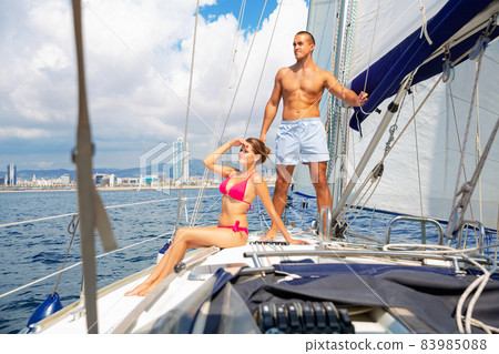 Young loving couple enjoying sea trip on pleasure sailboat along coast of Barcelona on sunny summer day Young loving couple enjoying sea trip on pleasure sailboat along coast of Barcelona on sunny summer day 83985088