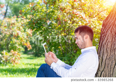 Young man using tablet computer under tree 83985268