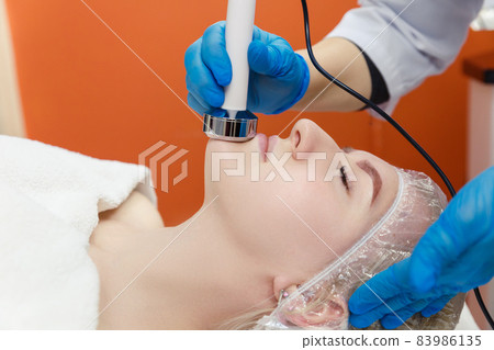 The process of cavitation on the face of a young woman. Rejuvenation and tightening of the skin of the face of hardware cosmetology. RF cavitation on the face. 83986135