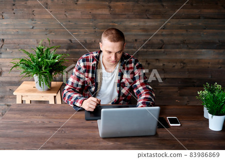 Photographer drawing and retouching image on laptop computer, using a digital tablet and stylus pen. Freelancer at the workplace in open space or coworking behind a laptop. Photographer drawing and retouching image on laptop computer, using a digital tablet and stylus pen. Freelancer at the workplace in open space or coworking behind a laptop. 83986869