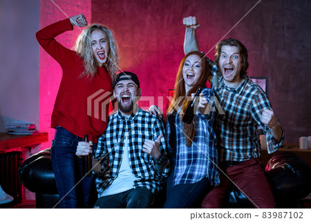 Four cheerful friends hanging out in an apartment and watching a Four cheerful friends hanging out in an apartment and watching a 83987102