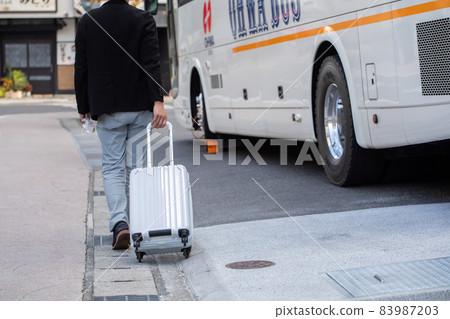 A man pulling a suitcase and heading for the bus 83987203