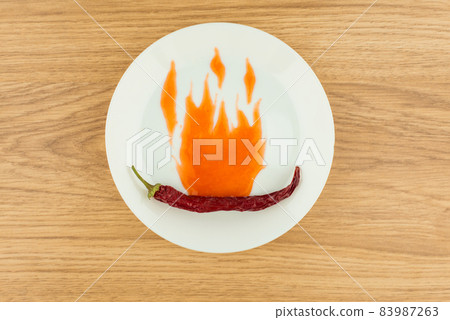 especially spicy sauce: dried chilli enveloped in flames drawn with a spicy chili sauce on a white plate , red wooden table especially spicy sauce: dried chilli enveloped in flames drawn with a spicy chili sauce on a white plate , red wooden table 83987263