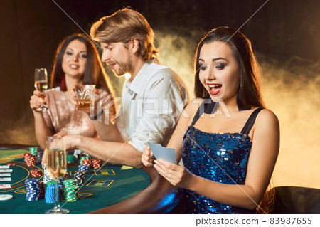 Group of an elegant people playing poker at the gambling house. Focus on a emotional brunette in a blue shiny dress 83987655