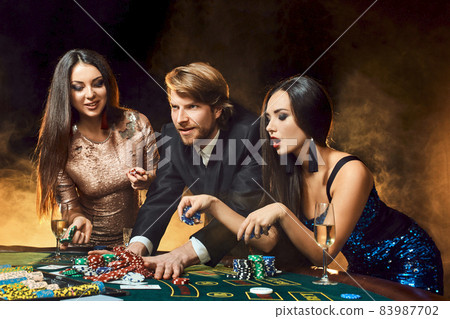 Two beautiful women and young man play on poker table in casino, focus on man and brunette Two beautiful women and young man play on poker table in casino, focus on man and brunette 83987702
