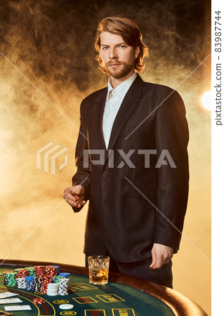 A man in a business suit standing near the game table. Male player. Passion, cards, chips, alcohol, dice, gambling, casino - it is as male entertainment. 83987744