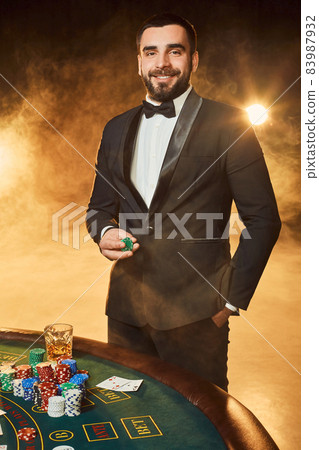 A young man in a business suit standing near poker table. Man gambles. 83987932