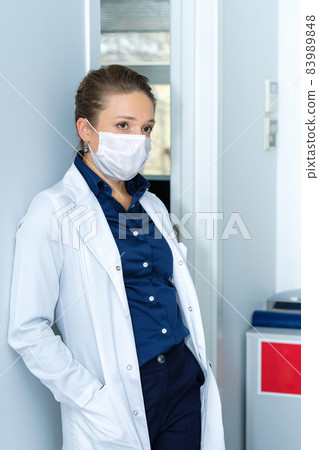 Portrait of a young female doctor in a medical mask and white medical coat. 83989848