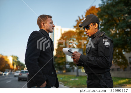 Male police officer issues a fine to driver 83990517