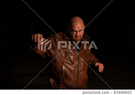 An angry man in a leather jacket attacks in the dark. An angry man in a leather jacket attacks in the dark. 83990602