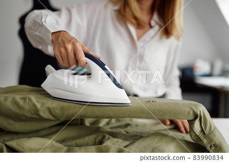 Seamstress smoothes fabric with an iron, workshop Seamstress smoothes fabric with an iron, workshop 83990834