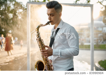 Male saxophonist plays melody on saxophone in park Male saxophonist plays melody on saxophone in park 83990984
