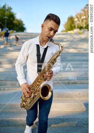 Saxophonist plays the saxophone on stairs in park 83991007