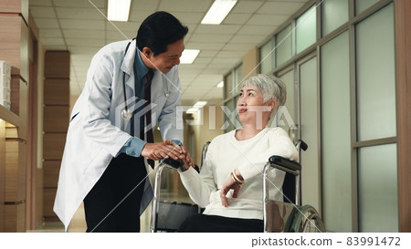 Doctor talking to elderly woman patient in wheelchair before surgery at hospital hallway 83991472