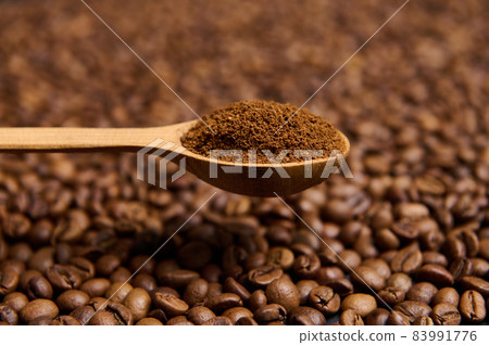 Close-up of a wooden spoon with ground coffee the background of scattered fresh roasted coffee beans with copy space for advertisement. Still life 83991776