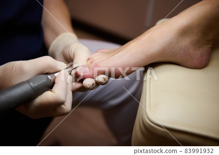Professional hardware pedicure using electric machine.Patient on pedicure procedure, visiting podiatrist.Peeling feet with special electric device.Foot treatment in SPA salon.Podiatry clinic. 83991932