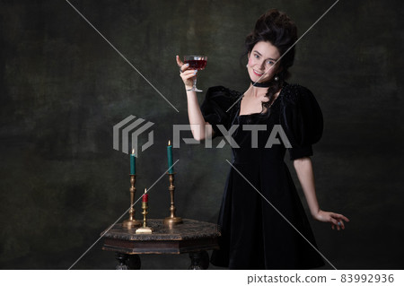 Classic retro portrait of young beautiful woman in image of medieval royal person in black dress isolated on dark vintage background. 83992936
