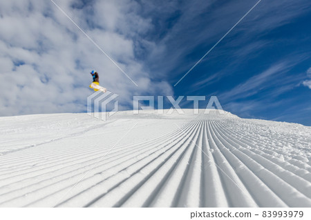 Close-up straight line rows of freshly prepared groomed ski slope piste with bright shining sun and clear blue sky background. Snowcapped mountain downhill landscape at europe winter skiing resort 83993979