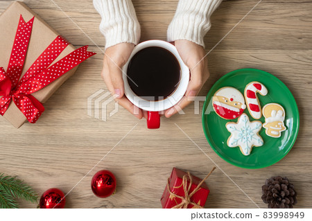 Merry Christmas with woman hand holding coffee cup and homemade cookie on table. Xmas eve, party, holiday and happy New Year concept 83998949