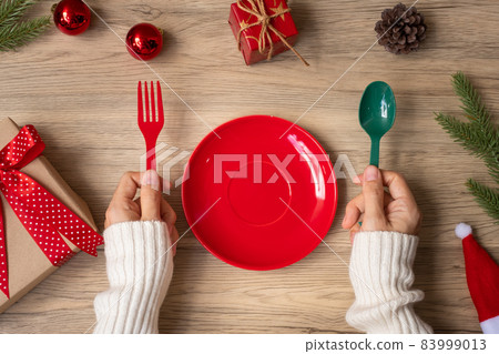 Merry Christmas with woman hand holding plate, fork and spoon on wood table background. Xmas, party and happy New Year concept 83999013