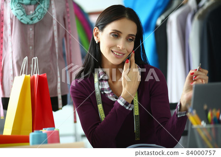 Female fashion designer accepts order on smartphone and discusses details of clothes in store 84000757