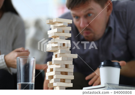 Man assembles a tall tower from wooden rectangular blocks 84000808