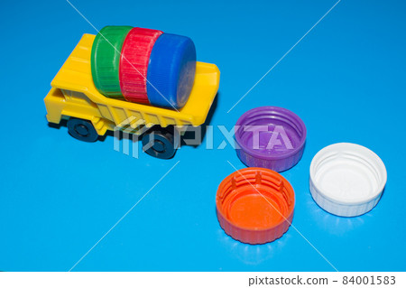 Toy dump truck unloads colorful plastic caps on blue background. Toy dump truck unloads colorful plastic caps on blue background. 84001583