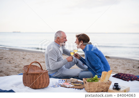 Happy senior couple in love sitting on blanket and having picnic outdoors on beach by sea. Happy senior couple in love sitting on blanket and having picnic outdoors on beach by sea. 84004063