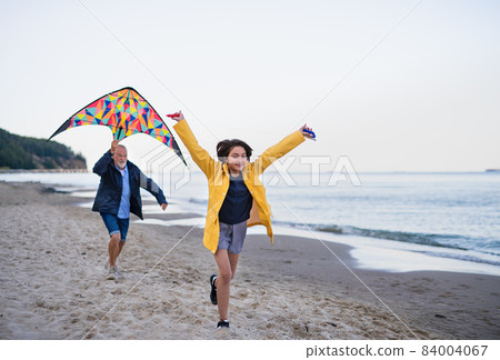 Senior man and his preteen granddaughter playing with kite on sandy beach. 84004067