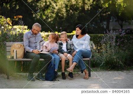 Senior couple with grandchildren sitting on bench and doing homewrok outdoors in park. Senior couple with grandchildren sitting on bench and doing homewrok outdoors in park. 84004165
