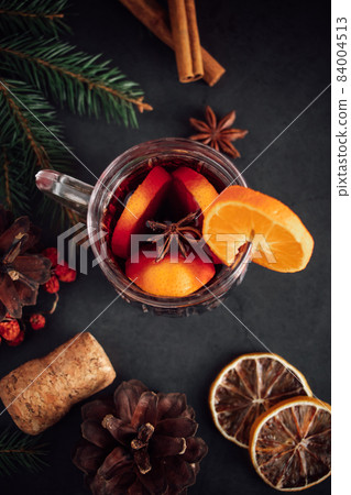Traditional Christmas warming mulled wine. Hot drink with spices in glass cup on a dark background. Traditional Christmas warming mulled wine. Hot drink with spices in glass cup on a dark background. 84004513