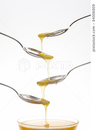 Fresh flower honey drips from a spoon into a spoon on a white background. Organic vitamin food. Fresh flower honey drips from a spoon into a spoon on a white background. Organic vitamin food. 84006809