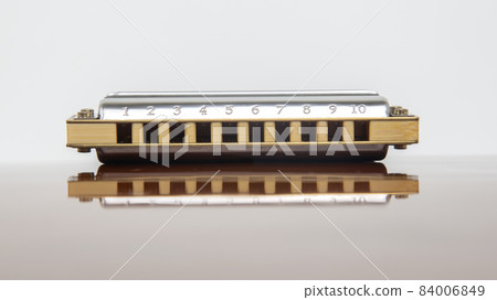 The harmonica lies on a mirrored surface. Classical musical wind instrument. 84006849
