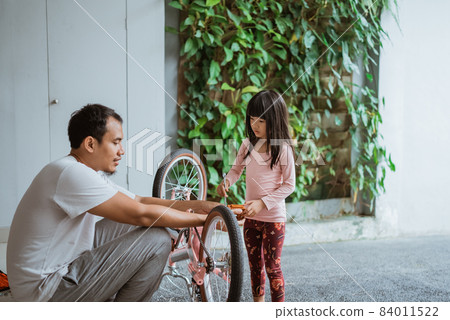 little girl holding a wrench while pedaling with her father little girl holding a wrench while pedaling with her father 84011522