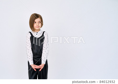 Little child girl in black white clothes stands over white background while looking sideways  84012932