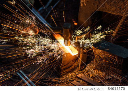 Blacksmith forging the molten metal on the anvil with spark fireworks Blacksmith forging the molten metal on the anvil with spark fireworks 84013370