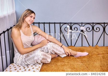 Hands-free Device for Home, phone holder is fixed on frame of metal bed, young woman is watching movie on screen of her smartphone. 84014208