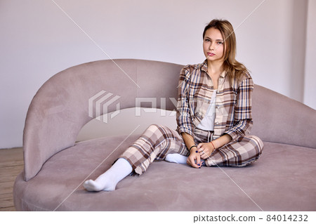 Woman in plaid suit, 24 years old, sits on couch. Woman in plaid suit, 24 years old, sits on couch. 84014232