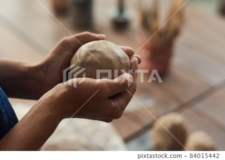 Hands of young woman holding spherical workpiece of clay 84015442
