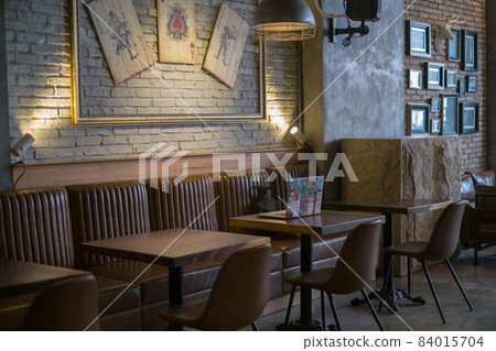 Laptop with stickers stands on a table in a coffee shop. Cafe design. Playing cards on the wall. High quality photo 84015704