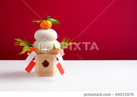 There is a photo of Kagami mochi (real rice cake) taken on a red and white background with the left side, Sanpo (pedestal). There is a photo of Kagami mochi (real rice cake) taken on a red and white background with the left side, Sanpo (pedestal). 84015876