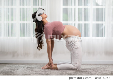 Happy Asian Pregnant woman using virtual reality glasses for practice yoga online class Ustrasana pose or yoga Camel pose to meditation smile with big belly relax at home. Pregnancy Technology Concept Happy Asian Pregnant woman using virtual reality glasses for practice yoga online class Ustrasana pose or yoga Camel pose to meditation smile with big belly relax at home. Pregnancy Technology Concept 84016032