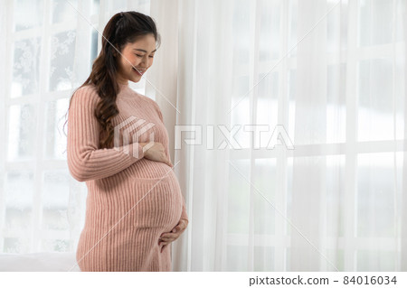 Happy Pregnant Woman standing in front of windows and stroking her big belly with love at cozy home,Pregnancy of young woman enjoy with future life relax with love,Motherhood and Pregnant Concept Happy Pregnant Woman standing in front of windows and stroking her big belly with love at cozy home,Pregnancy of young woman enjoy with future life relax with love,Motherhood and Pregnant Concept 84016034