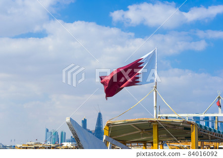 National flag of Qatar on a flagpole in front of blue sky 84016092