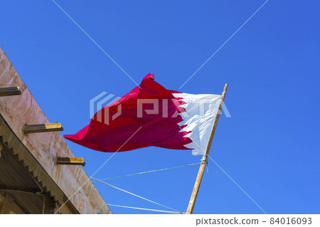 National flag of Qatar on a flagpole in front of blue sky 84016093